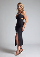 Front quarter image of a model wearing a black midaxi dress with a sweetheart neckline with wide straps, a side cut-out and front skirt split. The design featured is the Vesper Porticini Black Cut Out Midaxi Dress