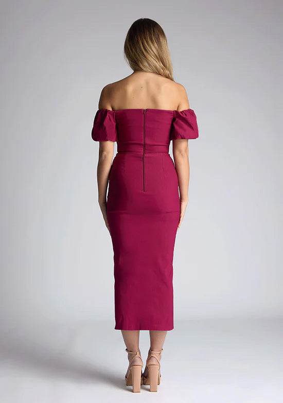 Back image of a blonde model wearing a berry midaxi dress with a bardot neckline gracefully frame off shoulders, while the back zip ensures a seamless silhouette. The dress  features is the Vesper Quinton Berry Midaxi Dress