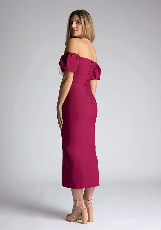 Back quarter image of a blonde model wearing a berry midaxi dress with a bardot neckline gracefully frame off shoulders, while the back zip ensures a seamless silhouette. The dress  features is the Vesper Quinton Berry Midaxi Dress