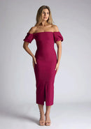 Front image of a blonde model wearing a berry midaxi dress with a bardot neckline gracefully frames the shoulders, while the back zip ensures a seamless silhouette. The dress  features is the Vesper Quinton Berry Midaxi Dress