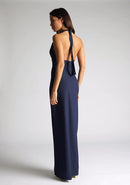 Back quarter  image of a blonde model wearing a navy maxidress with a v-plunging neckline, halter design and a front skirt split. The design featured is the Vesper Sedona Navy Maxi Dress