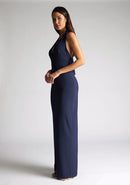 Front qaurter image of a blonde model wearing a navy maxidress with a v-plunging neckline, halter design and a front skirt split. The design featured is the Vesper Sedona Navy Maxi Dress