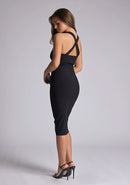 Back quarter image of a blonde model wearing a black sweetheart plunge midi dress with a plunge neckline with cross back detail and a slim fit. The design featured is the Vesper Sian Black Sweetheart Plunge Midi Dress