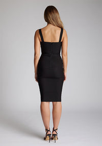 Back image of blonde model wearing a black midi pencil dress with a square neckline, slim fit and creating a silhoutte that's as chic as it is timeless. The design featured is the  Vesper Solara Black Midi Pencil Dress
