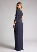 Back quarter image of a blonde model wearing a  Navy Maxi Dress with an asymmetric long-sleeve design, coupled with a tasteful front cutout, creates a uniquely stylish statement. The design features is the Vesper Vienna Navy One Sleeve Maxi Dress