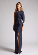 Front quarter image of a blonde model wearing a  Navy Maxi Dress with an asymmetric long-sleeve design, coupled with a tasteful front cutout, creates a uniquely stylish statement. The design features is the Vesper Vienna Navy One Sleeve Maxi Dress