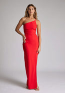 Front image of a model wearing a red maxi dress with a asymmetric neckline, one shoulder strap, front skirt split and open back with asymmetric strap across back. The design featured is Vesper Viva Red Maxi Dress