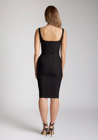 Back image of model wearing a  black pencil dress with a square-cut neckline and straps and a bodycon fit. The design features is the Vesper Zada Black Bodycon Pencil Midi Dress