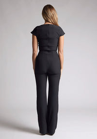 Back image of a model wearing a black jumpsuit with a square neckline and flattering v-wire design, this jumpsuit will have you feeling confident and stylish. The design features is the Vesper Zuri Black Wide Leg Jumpsuit