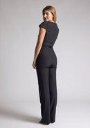 Back quarter image of a model wearing a black jumpsuit with a square neckline and flattering v-wire design, this jumpsuit will have you feeling confident and stylish. The design features is the Vesper Zuri Black Wide Leg Jumpsuit