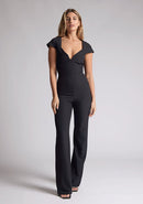 Front image of a model wearing a black jumpsuit with a square neckline and flattering v-wire design, this jumpsuit will have you feeling confident and stylish. The design features is the Vesper Zuri Black Wide Leg Jumpsuit